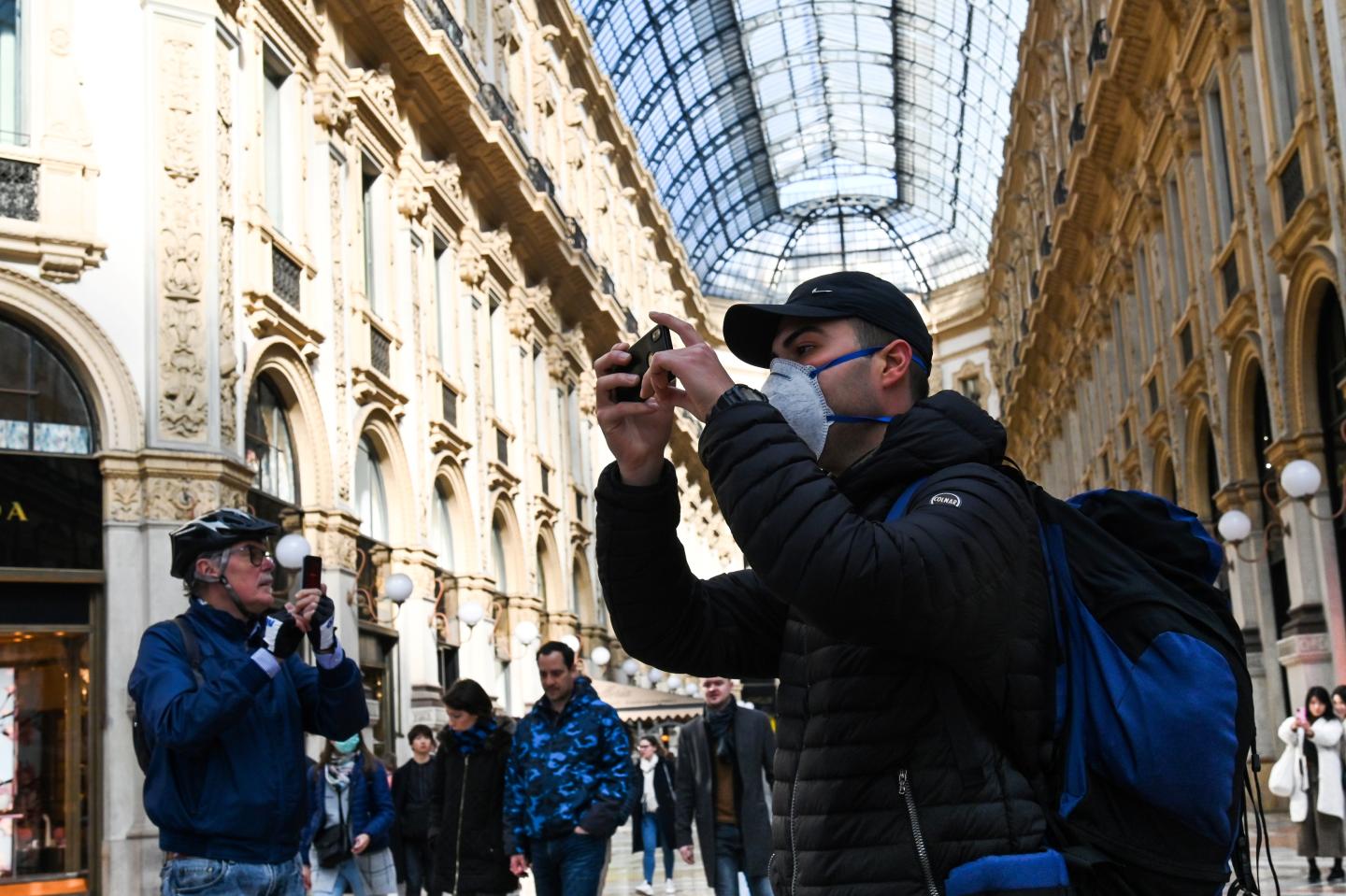 A man wearing a protective facemask takes pictures with his mobile phone at the Gallery Vittorio Emanuele II, in central Milan, on February 24, 2020 following security measures taken in northern Italy against the COVID-19 the novel coronavirus.