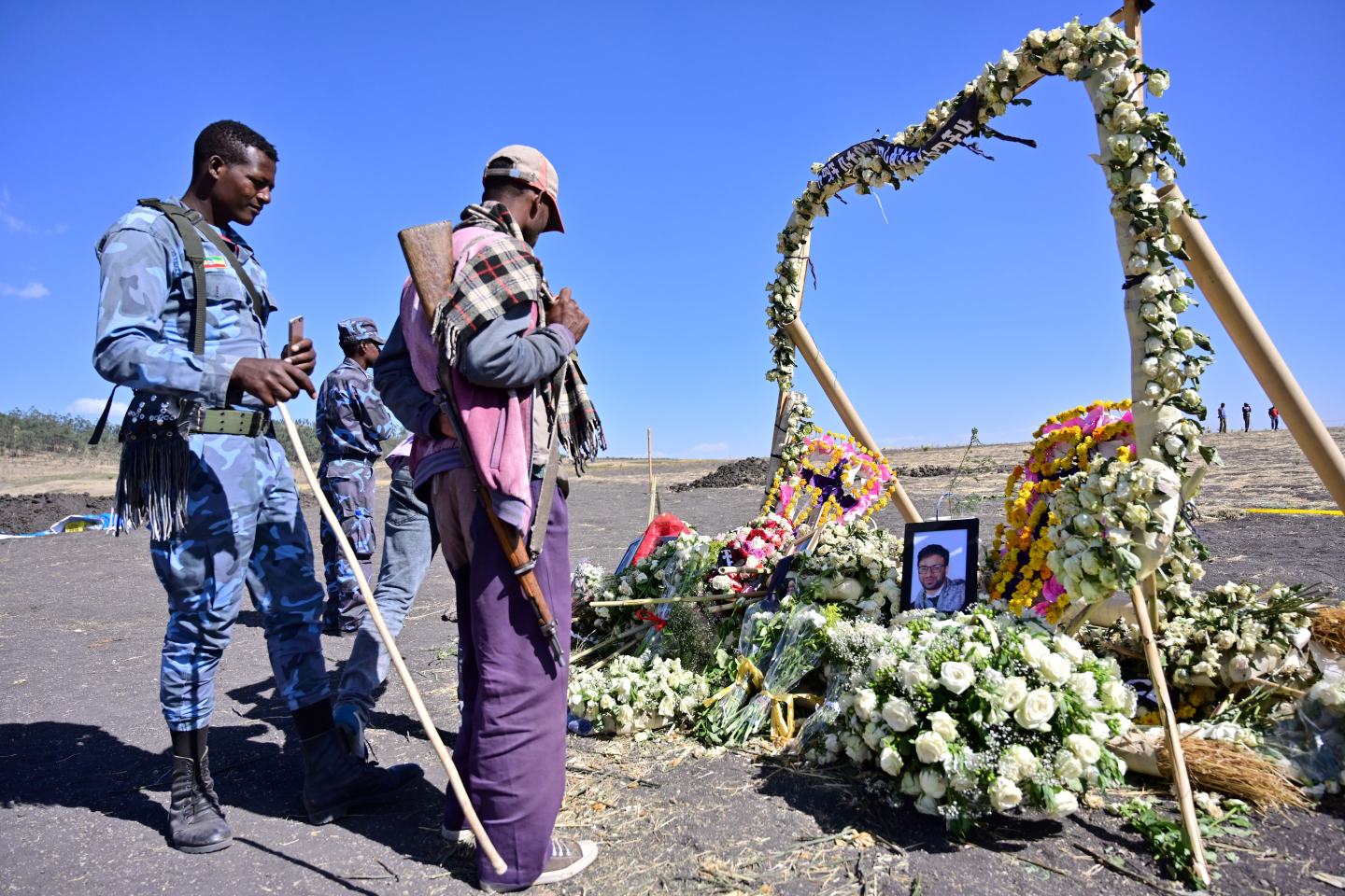 An ethiopian federal policeman and an Oromo tribesman look at a flower memorial bearing potraits of victims at the crash site of an Ethiopian airways operated Boeing 737 MAX aircraft on March 16, 2019 at Hama Quntushele village near Bishoftu in Oromia region. - A French investigation into the March 10 Nairobi-bound Ethiopian Airlines Boeing 737 MAX crash that killed 157 passengers and crew opened on March 15 as US aerospace giant Boeing stopped delivering the top-selling aircraft. (Photo by TONY KARUMBA / AFP) (Photo credit should read TONY KARUMBA/AFP via Getty Images)