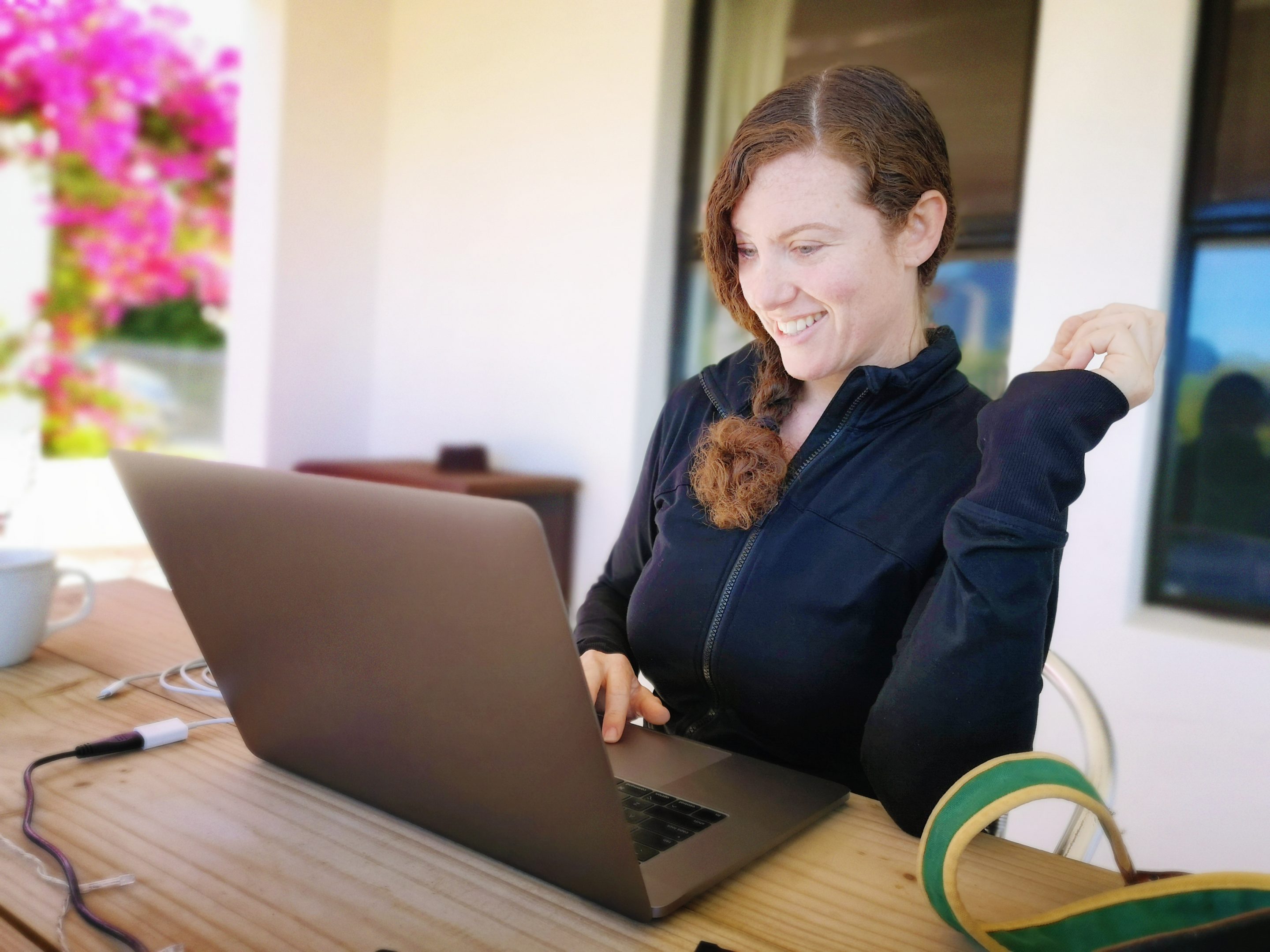 Female freelancer enjoying work on her laptop from her patio. She smiles with delight at the results of fer efforts.