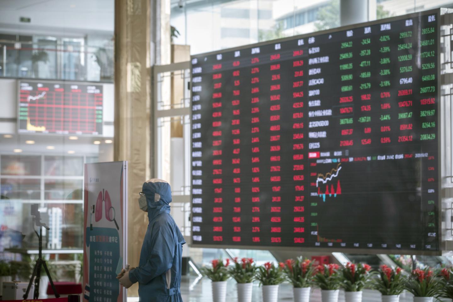 A worker wearing a protective suit stands at a temperature screening point in front of an electronic stock board at the Shanghai Stock Exchange in Shanghai, China, on Monday, March 2, 2020. The pressure to get China back to work after the coronavirus shutdown is resurrecting an old temptation: doctoring data so it shows senior officials what they want to see. Photographer: Qilai Shen/Bloomberg via Getty Images