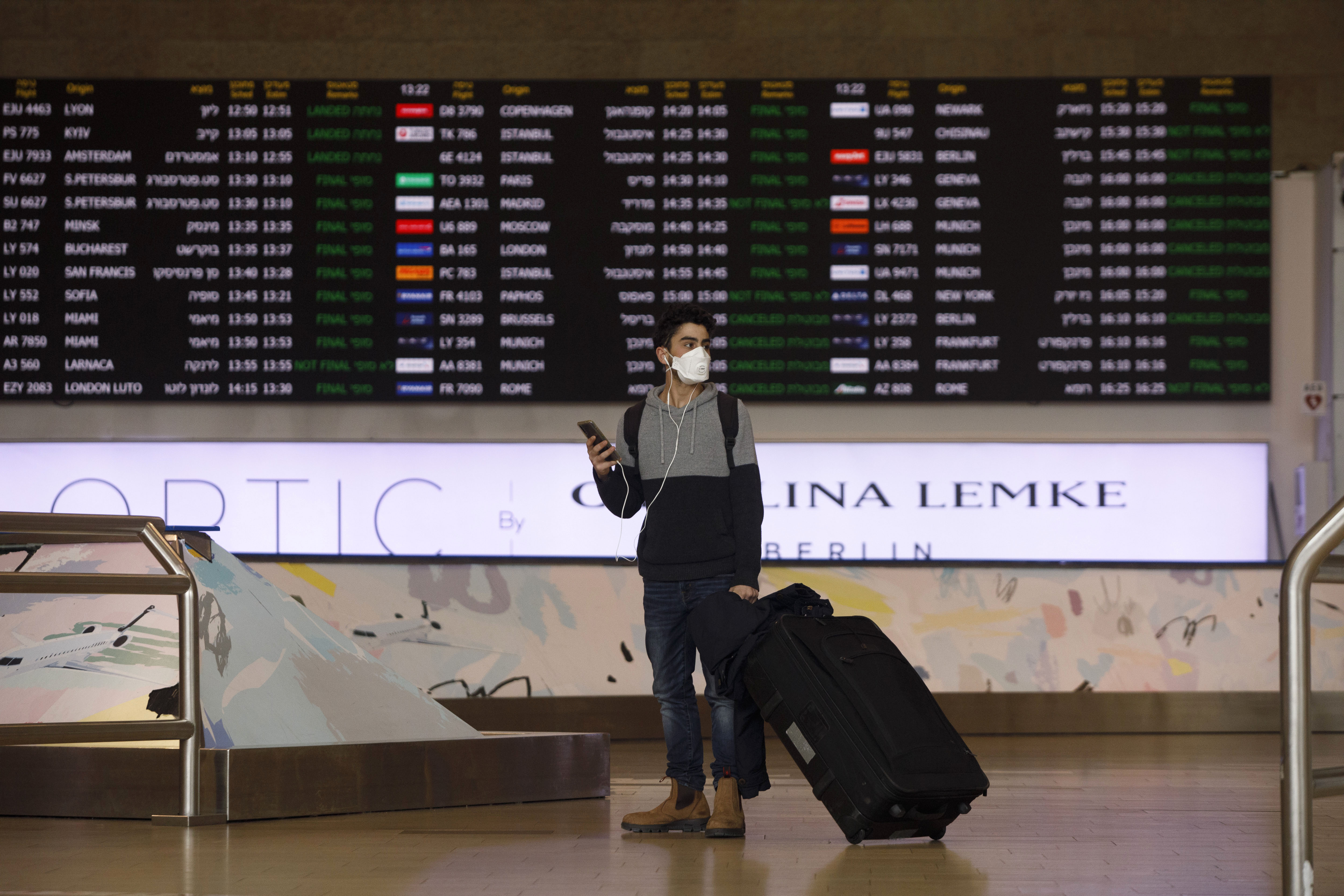 An airline passenger wearing a protective face mask pauses with his smartphone in the arrivals hall at Ben Gurion International airport in Tel Aviv, Israel, on Tuesday, March 10, 2020.