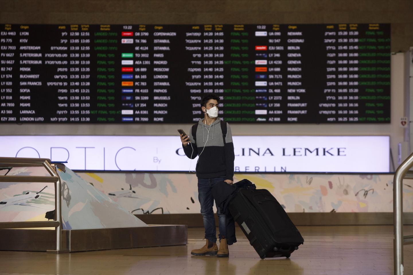 An airline passenger wearing a protective face mask pauses with his smartphone in the arrivals hall at Ben Gurion International airport in Tel Aviv, Israel, on Tuesday, March 10, 2020.