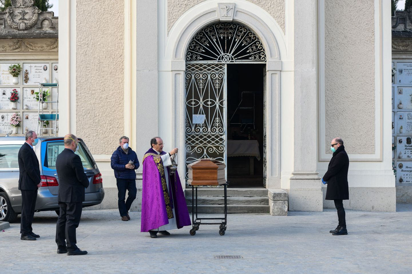 A man wearing a face mask (R) stands by the coffin of his mother as a priest swings a thurible of incense and undertakers look on during a funeral service in the closed cemetery of Seriate, near Bergamo, Lombardy, Italy, on March 20, 2020.