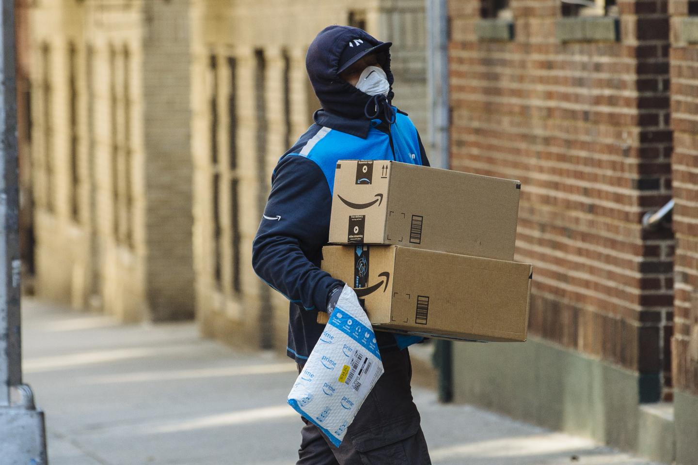 A worker wearing a protective mask and gloves carries Amazon.com Inc. boxes during a delivery in the Bronx borough of New York, U.S., on Thursday, March 26, 2020. New York City is the epicenter of the coronavirus pandemic in the United States, putting historic pressure on a world-renowned healthcare system as the number of confirmed cases in the area grows exponentially. Photographer: Angus Mordant/Bloomberg via Getty Images