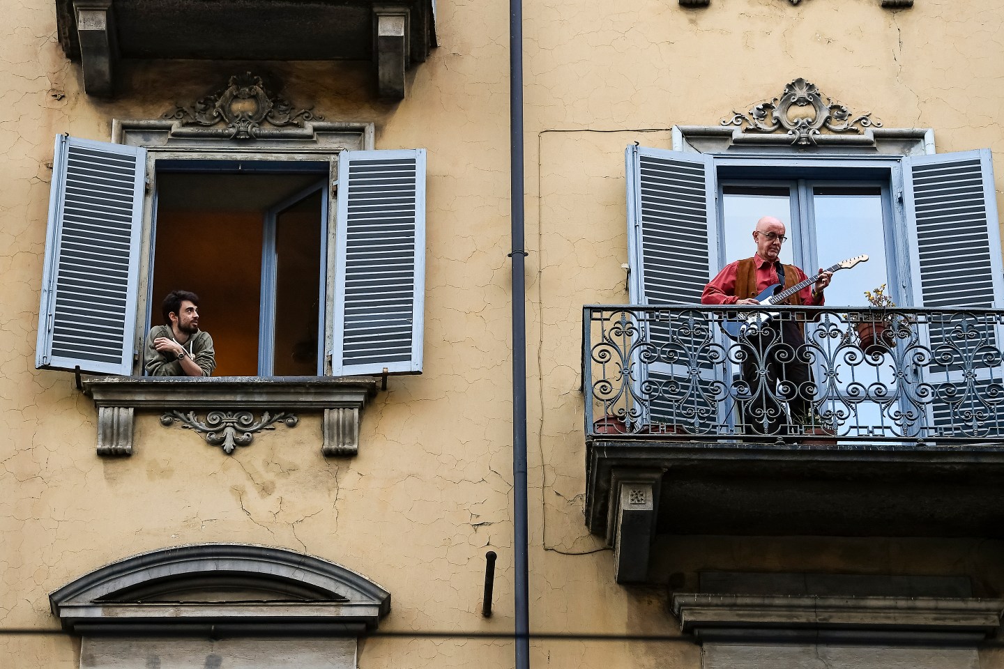 A man plays guitar from the balcony of his home as a man
