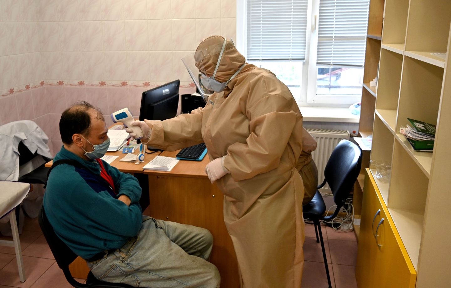 A doctor wearing protective gear measures the body temperature of a man, suspected of being infected with the COVID-19 coronavirus, at a clinic in the Ukrainian town of Irpin outside Kiev on April 15, 2020. (Photo by Sergei SUPINSKY / AFP) (Photo by SERGEI SUPINSKY/AFP via Getty Images)