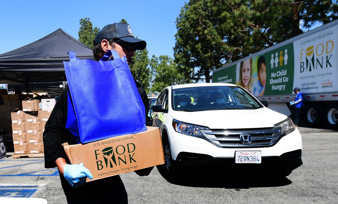Volunteers help load food into vehicles arriving at a Los Angeles Regional Food Bank drive-thru giveaway in Pico Rivera, California on April 28, 2020. - An estimated 3,000 families are facing food and/or economic difficulties due to the COVID-19 pandemic as California processes 3.2 million unemployment claims since March 15.