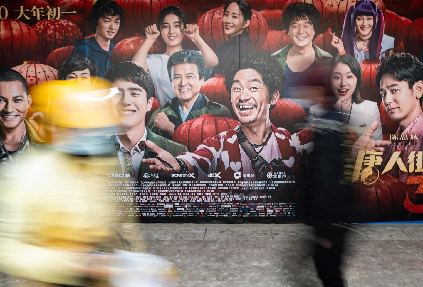 Pedestrians walk past a poster of movie 'Detective Chinatown' amid the coronavirus outbreak on March 28, 2020 in Beijing, China.