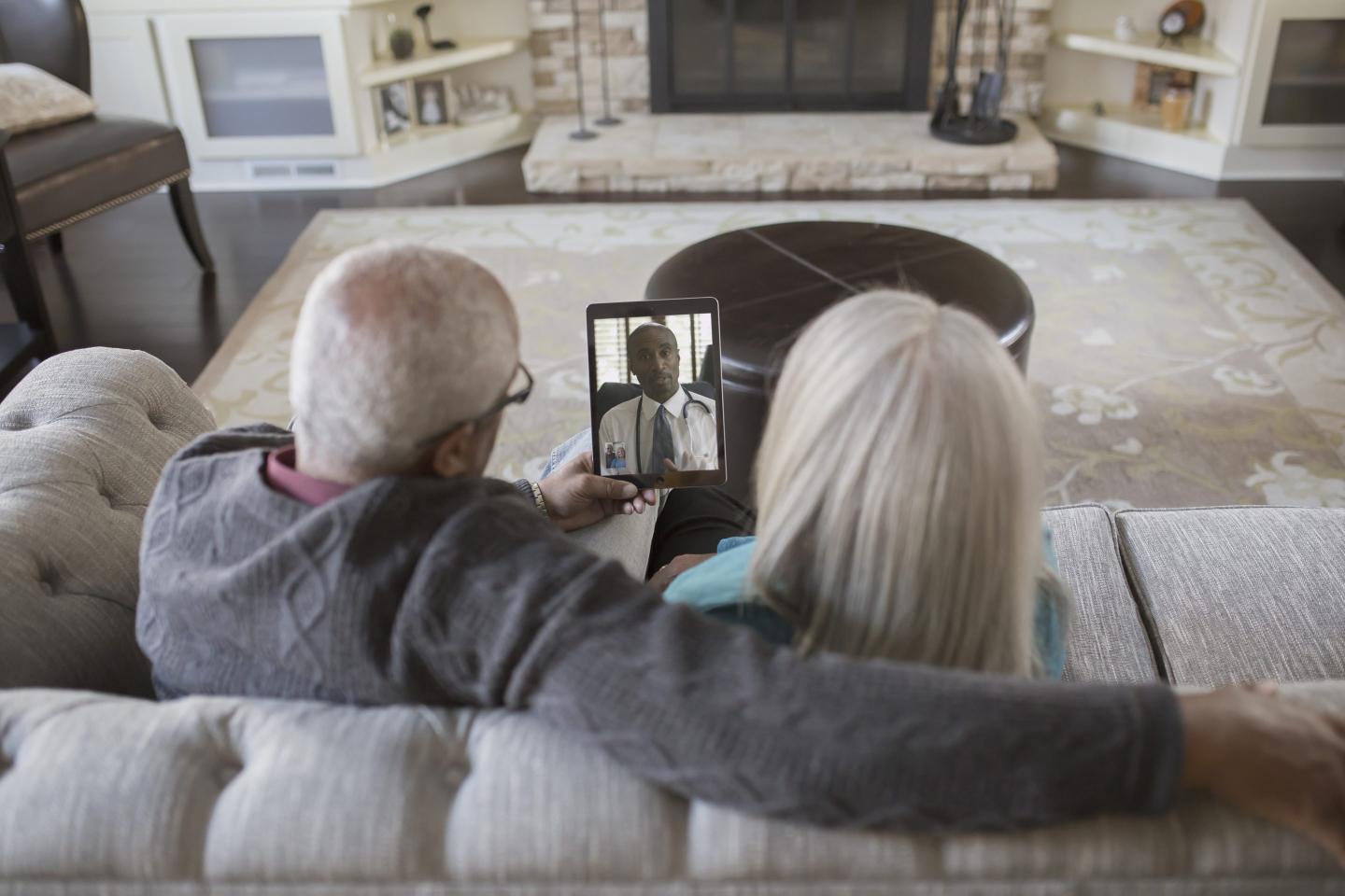 Elderly couple on couch during a telehealth appointment.