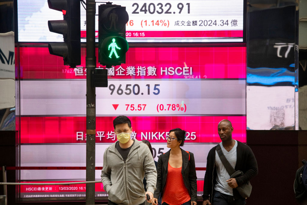 Pedestrians walk past a stock market display board showing