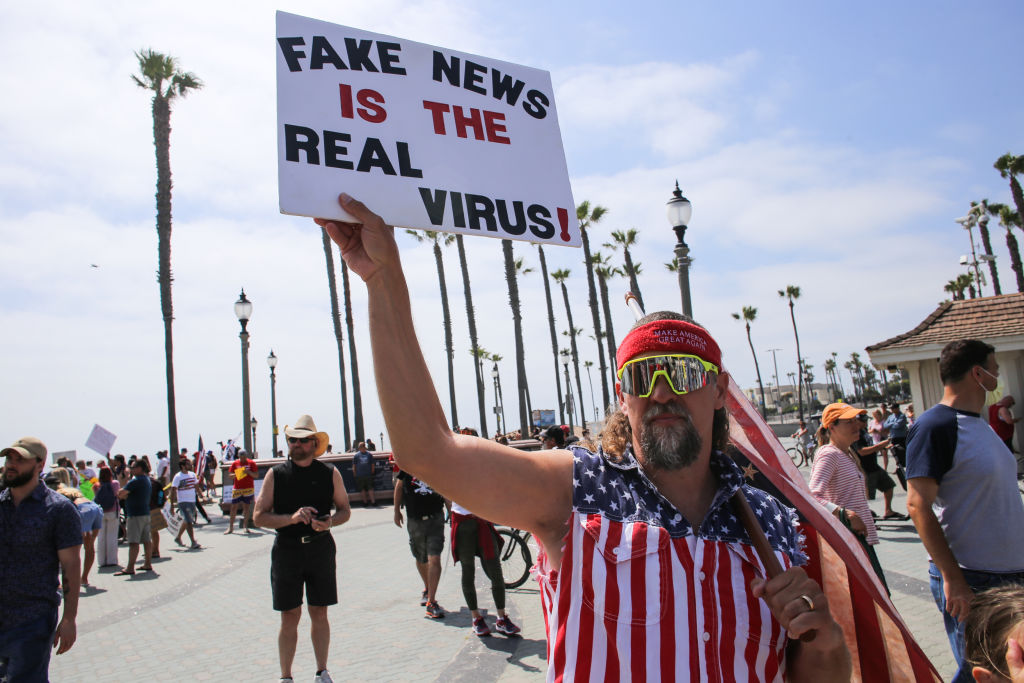 A protester holds a placard that says Fake News Is The Real Virus