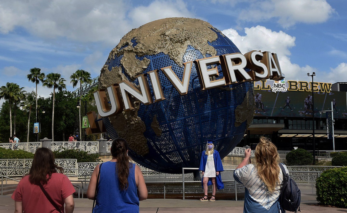 A graduate wearing a cap, gown, and face mask poses for a photograph at Universal Orlando's CityWalk in May 2020.