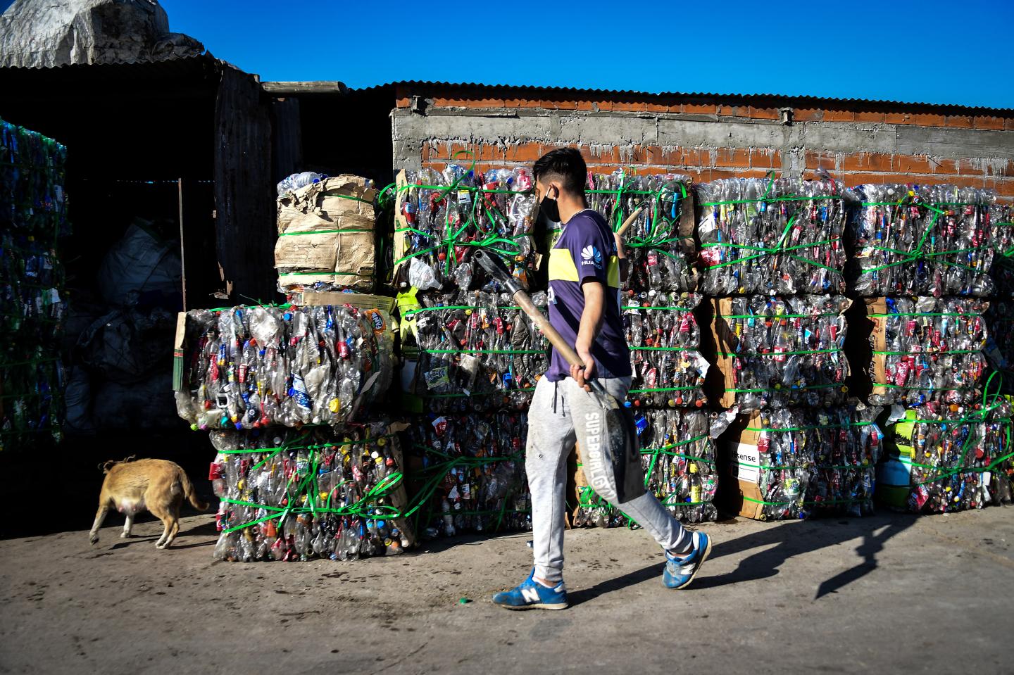 A man wearing a face mask and holding a shovel walks by compacted plastic bottles for recycling at Villa Itati on May 28, 2020 in Quilmes, Argentina.