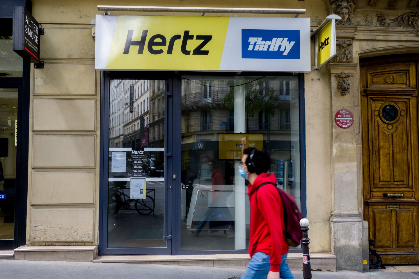 A passerby wearing a protective face mask walks past a closed Hertz car rental shop at Boulevard Saint-Michel, on May 23, 2020 in Paris, France.