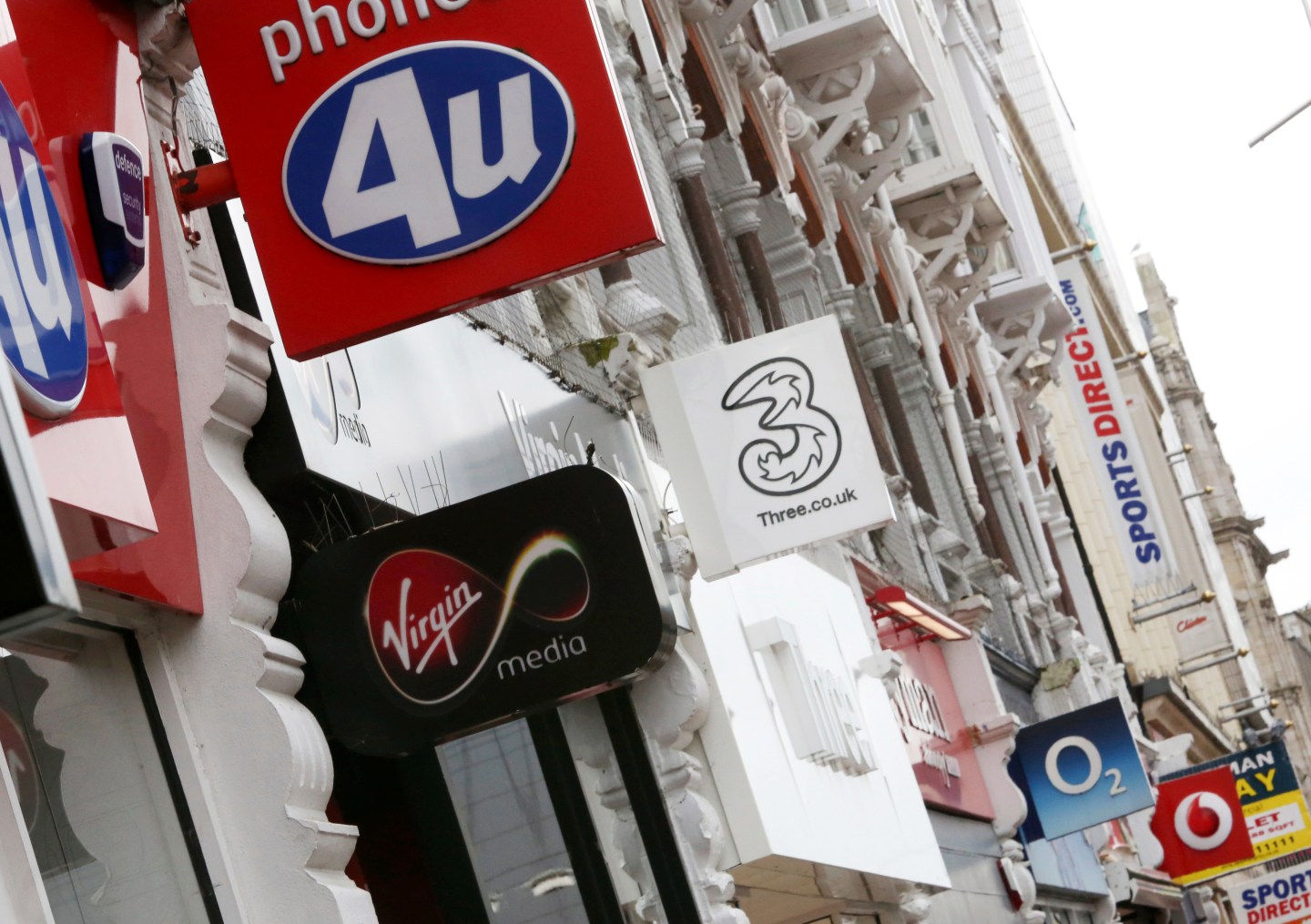 A row of mobile phone company logos are displayed on a British high street in Southend, U.K. On Thursday, Telefonica's O2 agreed to merge with Virgin Media, part of John Malone's sprawling Liberty Global telecommunications group, creating a $38 billion giant. Wire photography: Chris Ratcliffe—Bloomberg via Getty Images