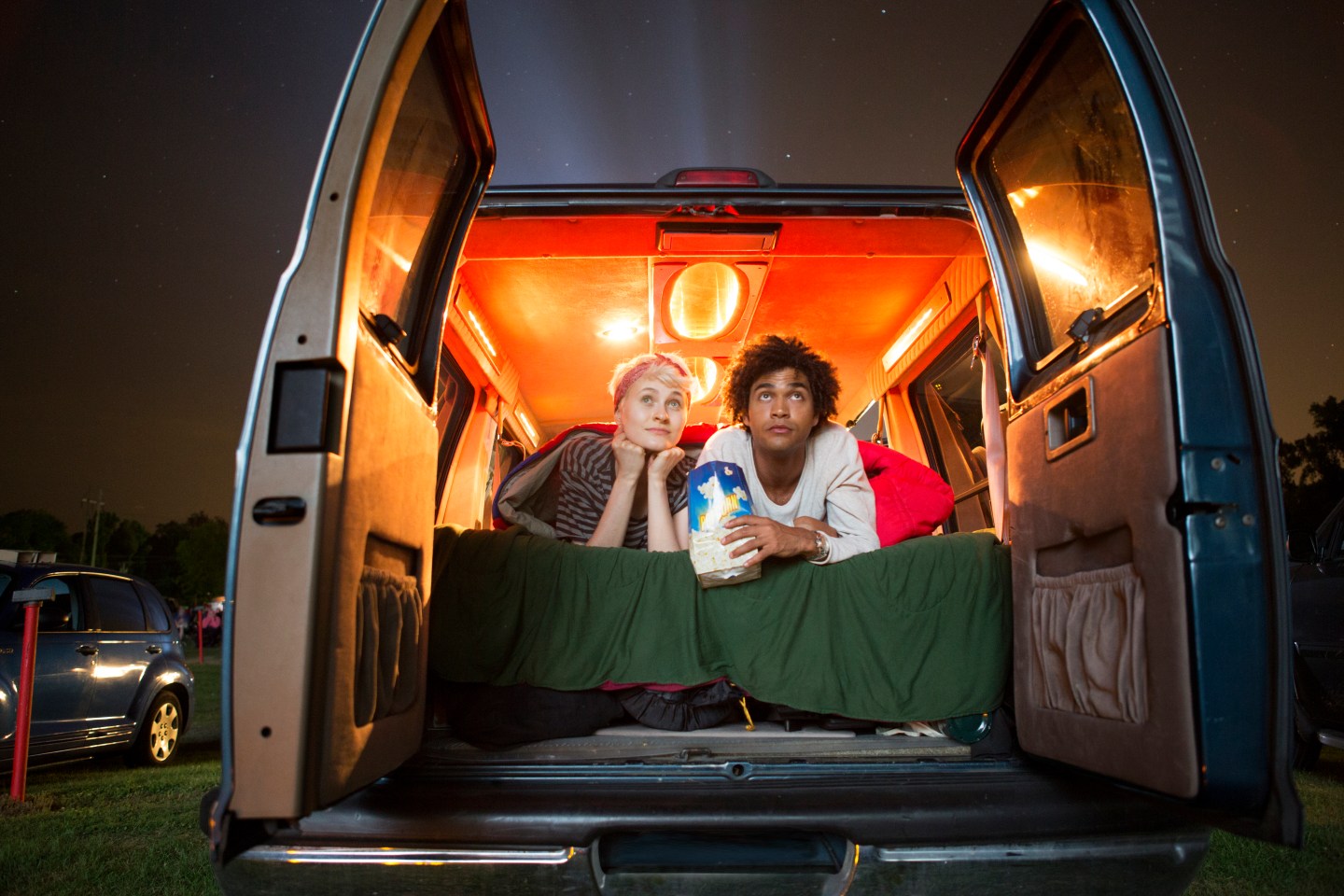 Couple holding popcorn while sitting in camping van during drive-in movie