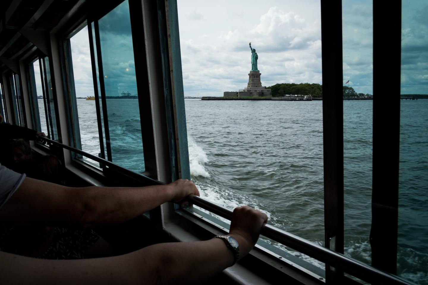 People hold onto a railing as they ride a ferry toward Liberty Island and the Statue of Liberty, August 8, 2017 in New York City.