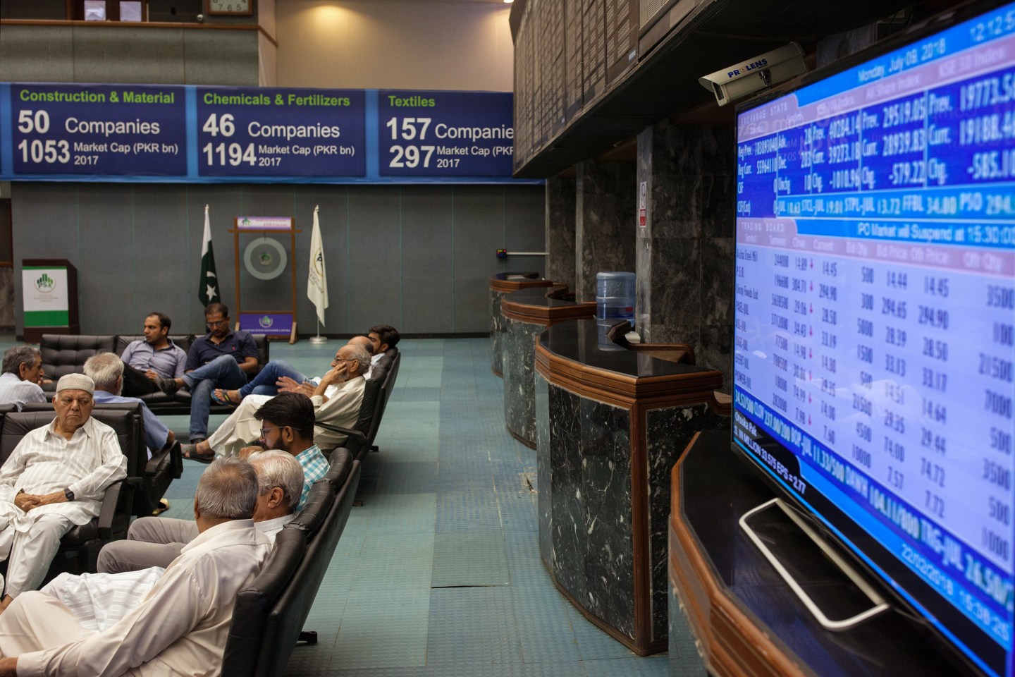 People sit next to a monitor displaying stock prices during a trading session at the Pakistan Stock Exchange in Karachi, Pakistan in 2018. On Monday, gunmen tried to storm the complex housing the stock exchange, leading to a deadly exchange of fire. Wire photography: Asim Hafeez/Bloomberg via Getty Images