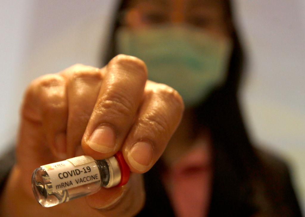 A researcher holds a COVID-19 mRNA vaccine during a news