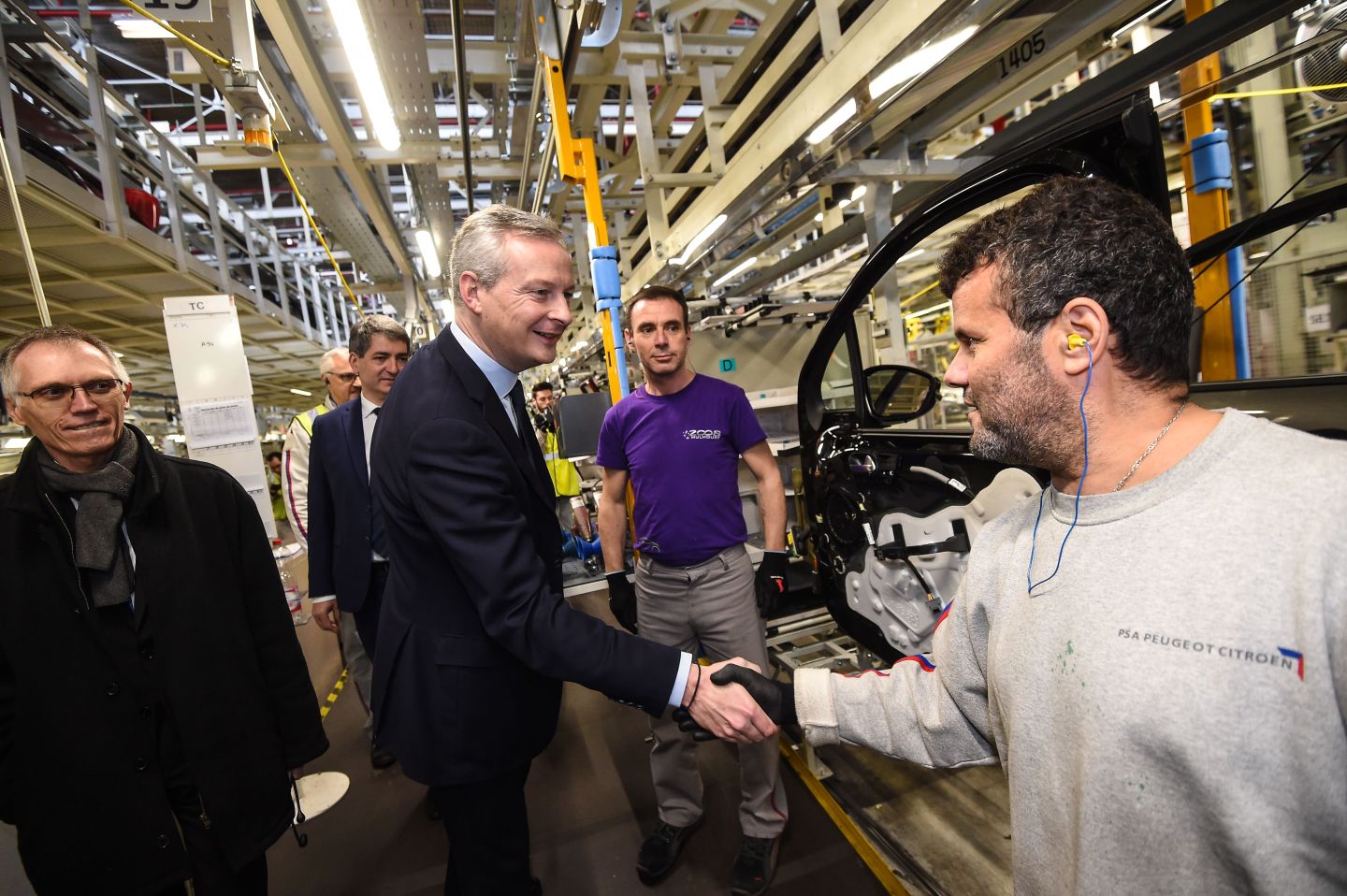 French Economy Minister Bruno Le Maire (C) shakes hands with a PSA Peugeot Citroen employee, flanked by chairman of the managing board of French carmaker PSA Peugeot Citroen Carlos Tavares (L), during a visit to the PSA car plant in Mulhouse on February 23, 2018.