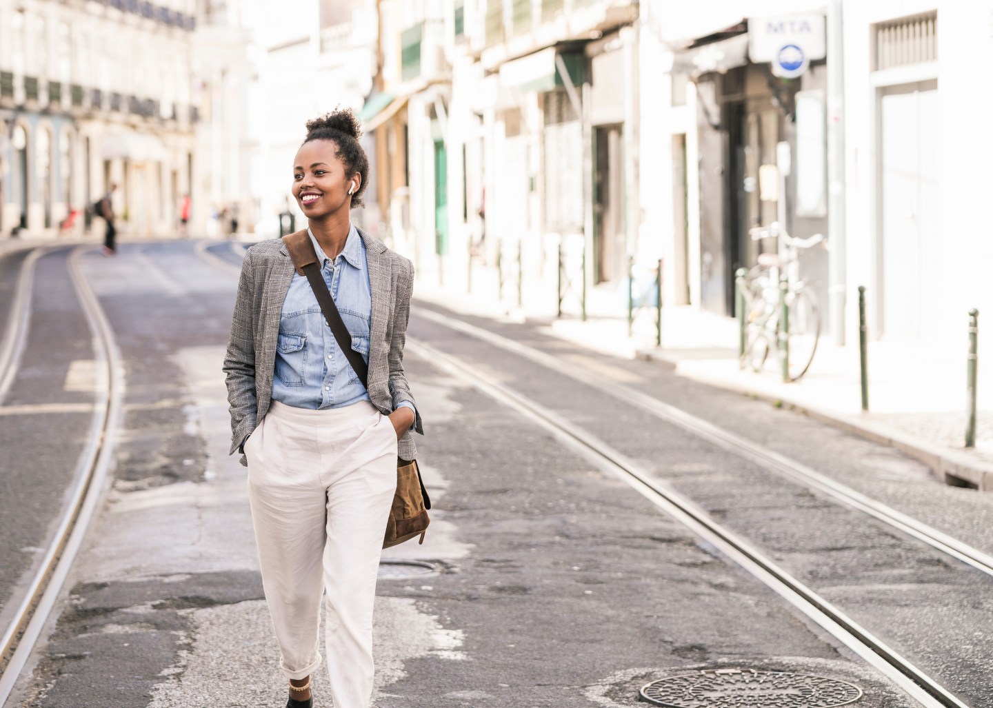 Smiling young woman with wireless earphones in the city on the go, Lissabon, Portugal