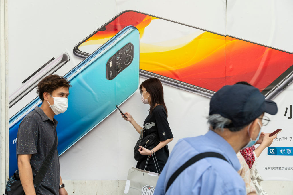 Commuters wearing face masks pass by a Xiaomi smartphone