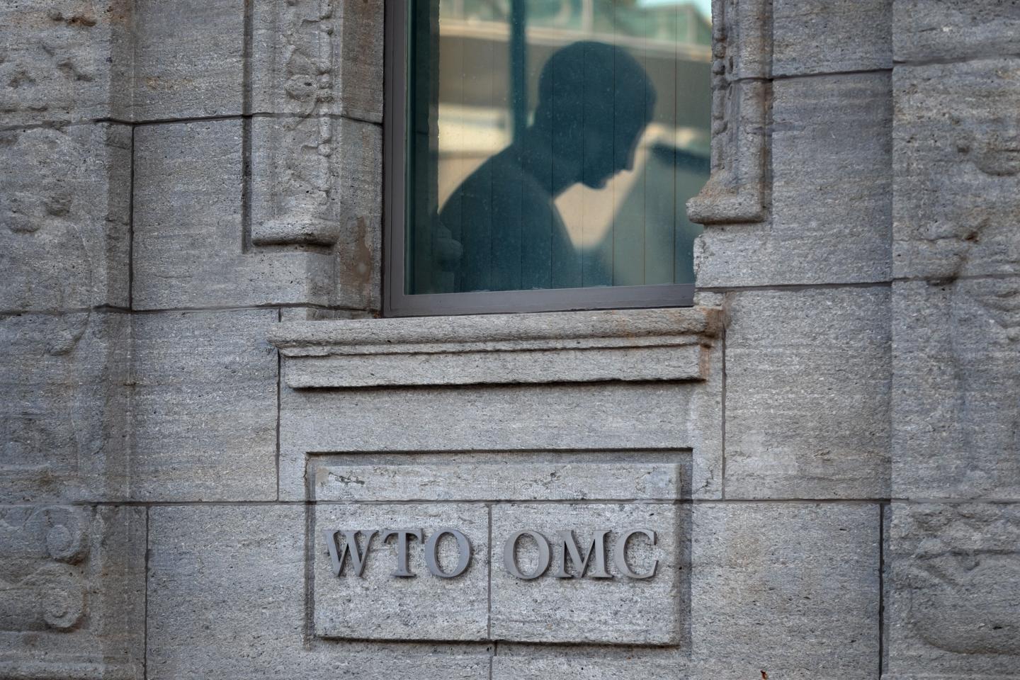 A picture taken on July 23, 2020 shows the silhouette of a statue reflected in a window above a sign at the entrance of the World Trade Organization (WTO) prior to a general council in Geneva.