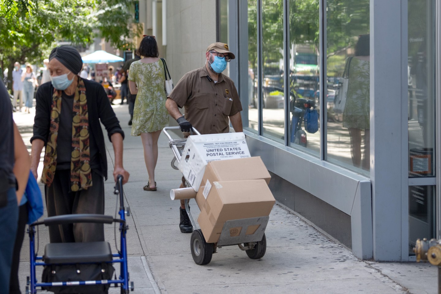 A UPS worker wearing a mask walks with a USPS plastic tub and packages near Union Square as the city continues Phase 4 of re-opening following restrictions imposed to slow the spread of coronavirus on August 18, 2020 in New York City.