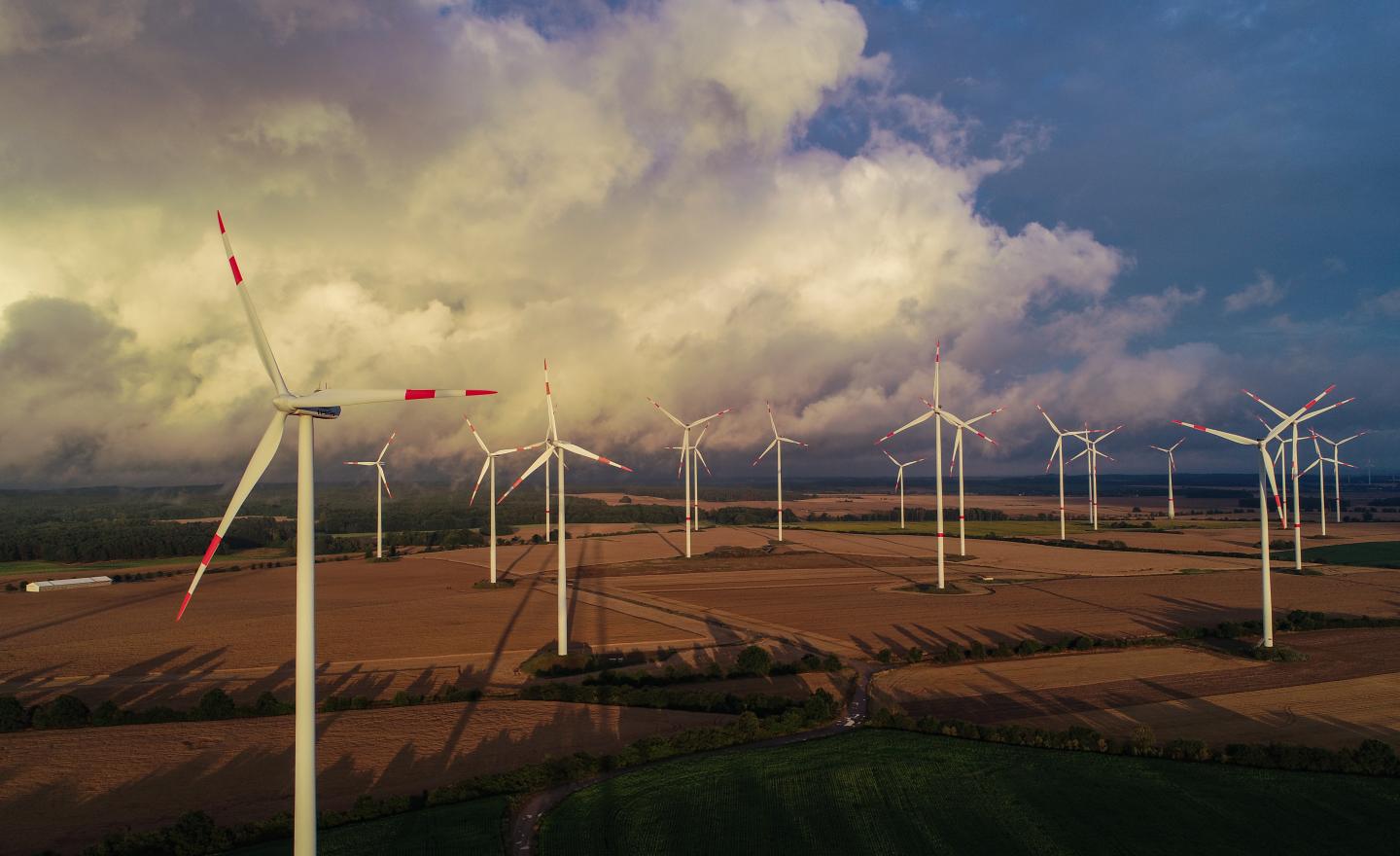 15 July 2020, Brandenburg, Germany: The light of the low-lying evening sun shines over wind turbines in the "Odervorland" wind farm in the Oder-Spree district (aerial photograph taken with a drone).