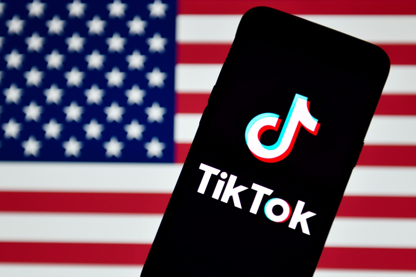 In this photo illustration a TikTok logo is seen displayed on a smartphone with the USA flag in the background.