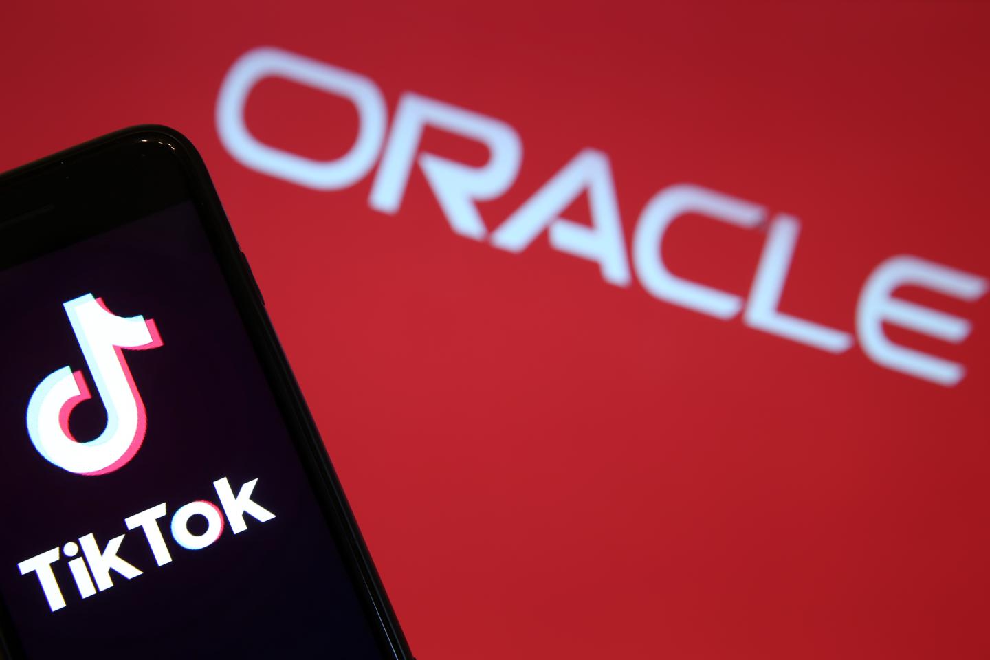 In this photo illustration the logo of Chinese media app for creating and sharing short videos TikTok, also known as Douyin is displayed on the screen of a smartphone in front of a TV screen displaying an Oracle logo on September 15, 2020 in Paris, France.