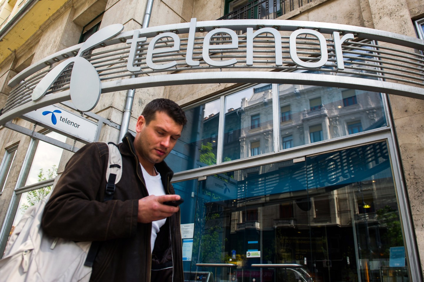 A pedestrian checks his mobile handset while passing a Telenor ASA mobile phone store in Budapest, Hungary, on Tuesday, April 24, 2012.