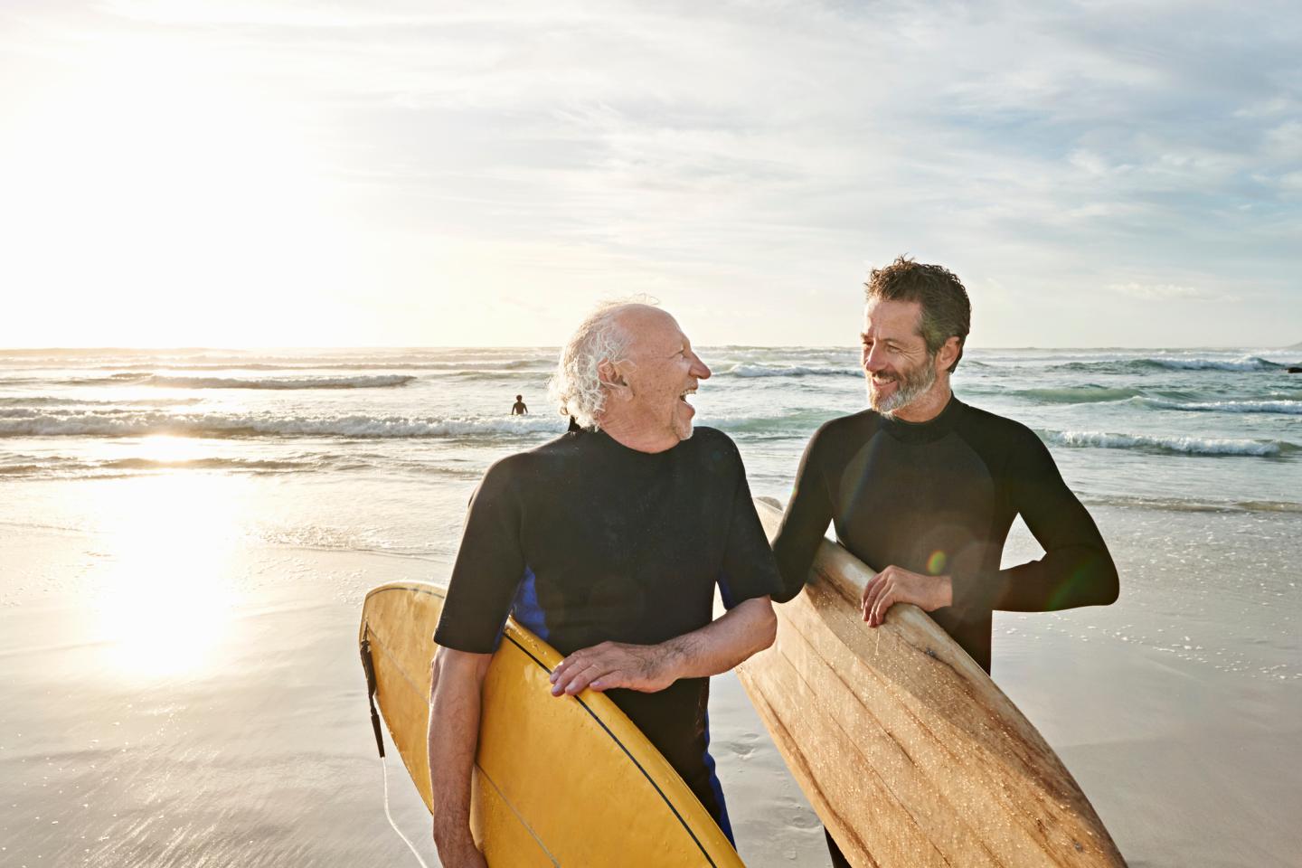 Father and his adult son on a beach with matching surf boards.