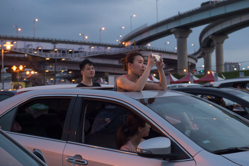 A father and son sit in their car while watching a movie at