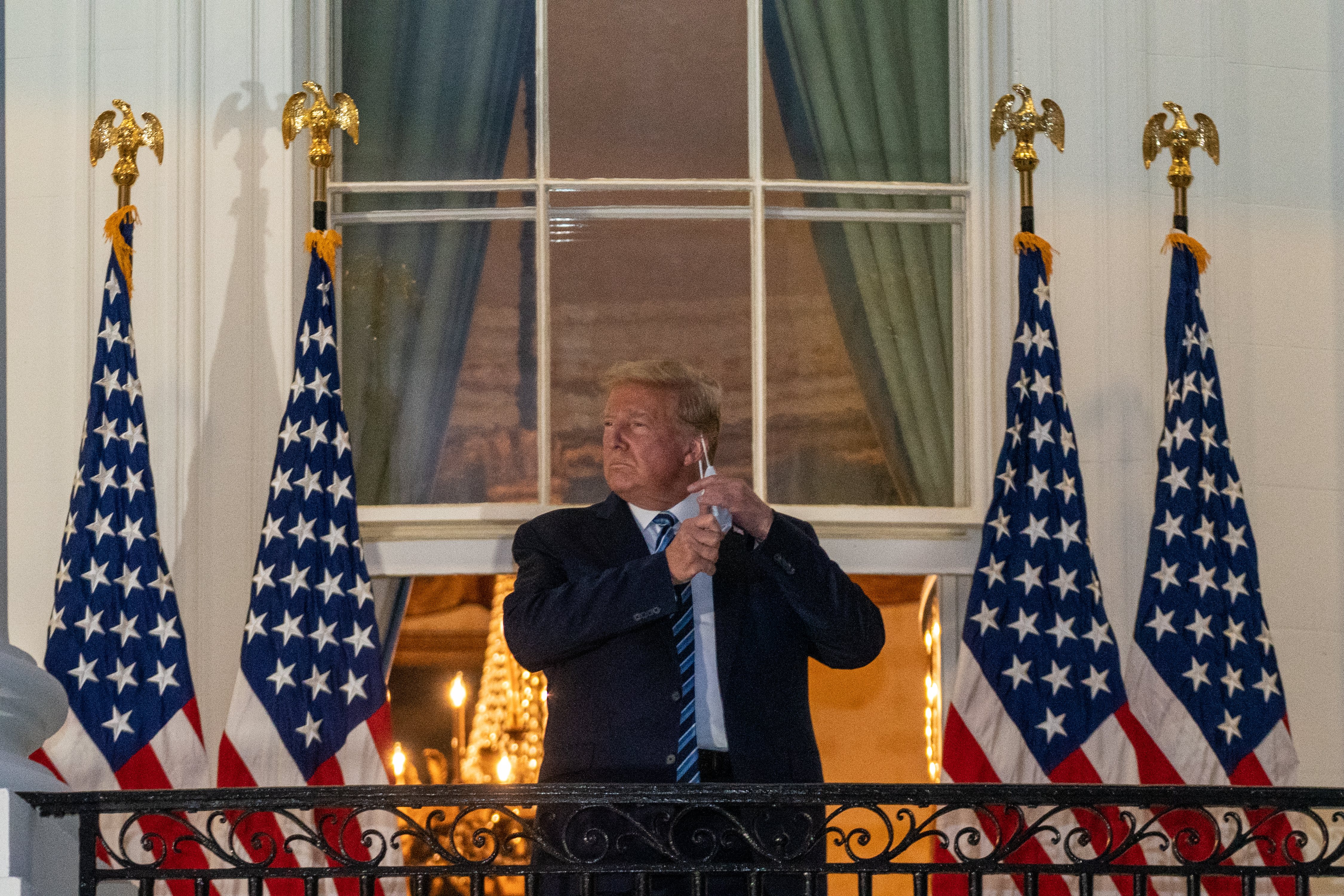 U.S. President Donald Trump removes his protective mask on the Truman Balcony of the White House in Washington, D.C., U.S., on Monday, Oct. 5, 2020. Trump's aides will try to keep him confined to the White House residence after being discharged from the hospital with Covid-19 but are unsure they can limit his movements. Ken Cedeno/Polaris/Bloomberg via Getty Images 