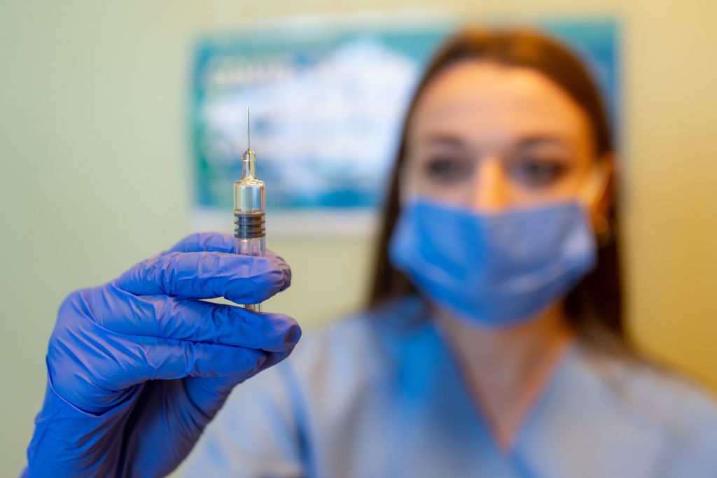A masked and gloved healthcare worker holding a syringe.
