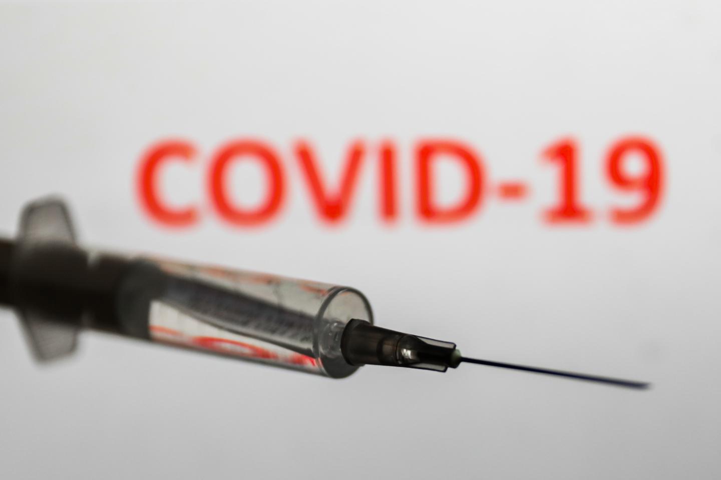 Medical syringe is seen with 'covid-19' sign displayed on a screen in the background in this illustration photo taken in Poland on October 12, 2020.