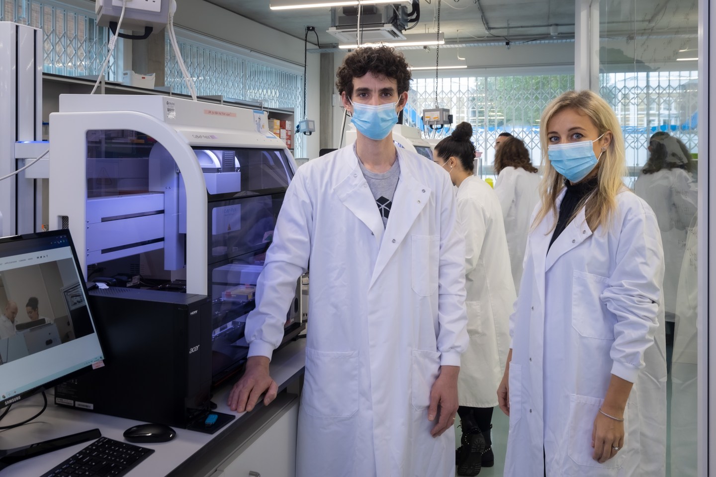 Photo of LabGenius founder and CEO James Field and Atomico partner Irina Haivas standing in the company's robotic lab wearing white lab coats and surgical masks.