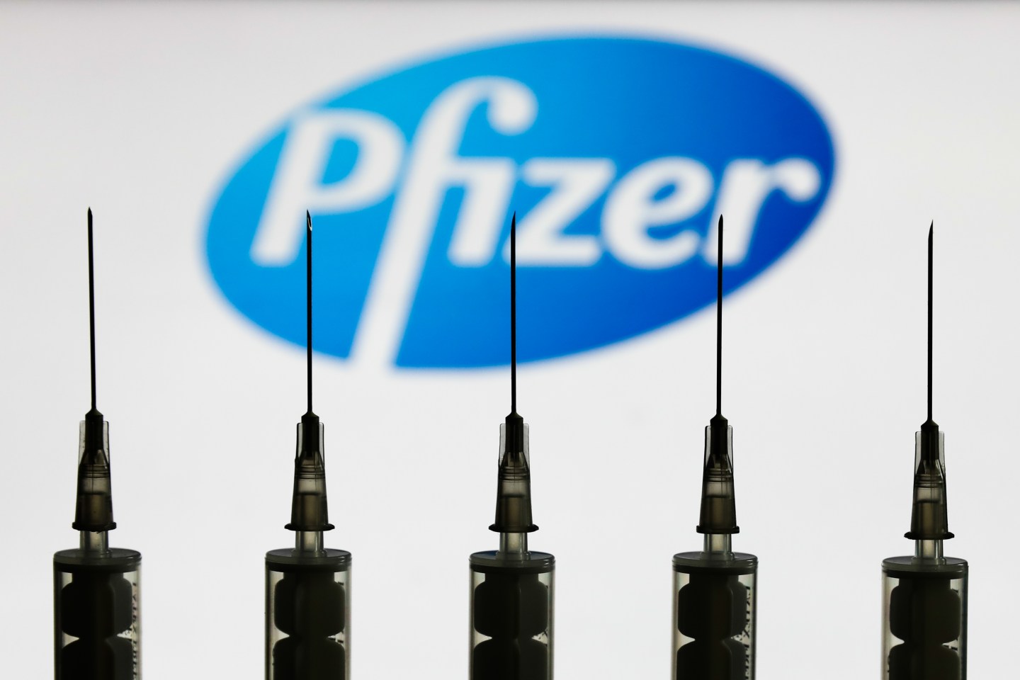 Medical syringes are seen with Pfizer company logo displayed on a screen in the background in this illustration photo taken in Poland on October 12, 2020.