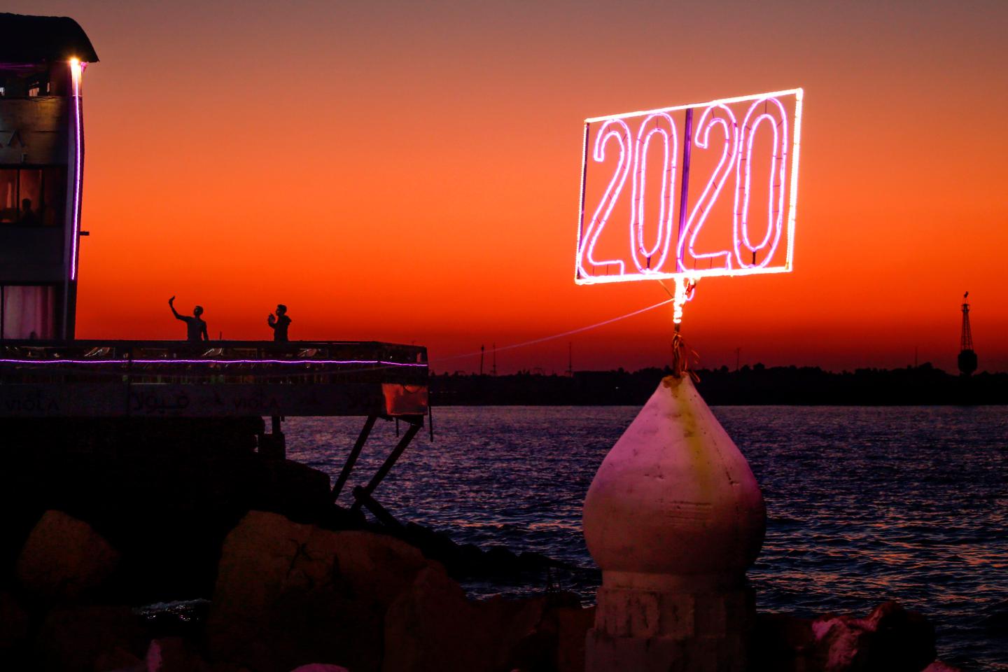 Palestinian youths pose for a "selfie picture" by the Mediterranean sea waterfront in Gaza City on December 23, 2019, a with a neon sign reading "2020" in the foreground.
