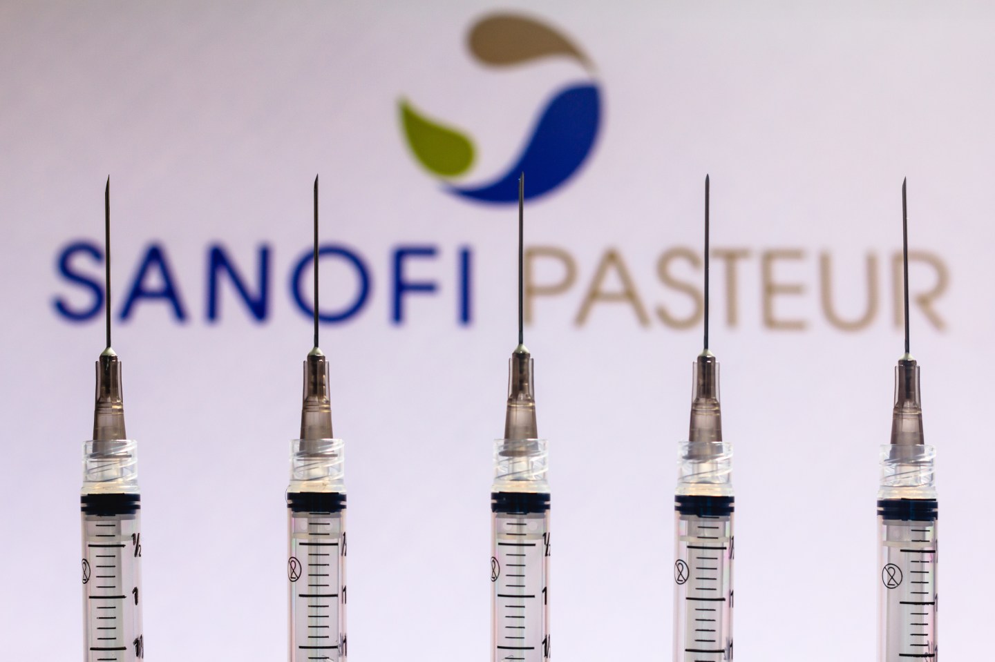 In this photo illustration various medical syringes seen with Sanofi Pasteur company logo displayed on a screen in the background.