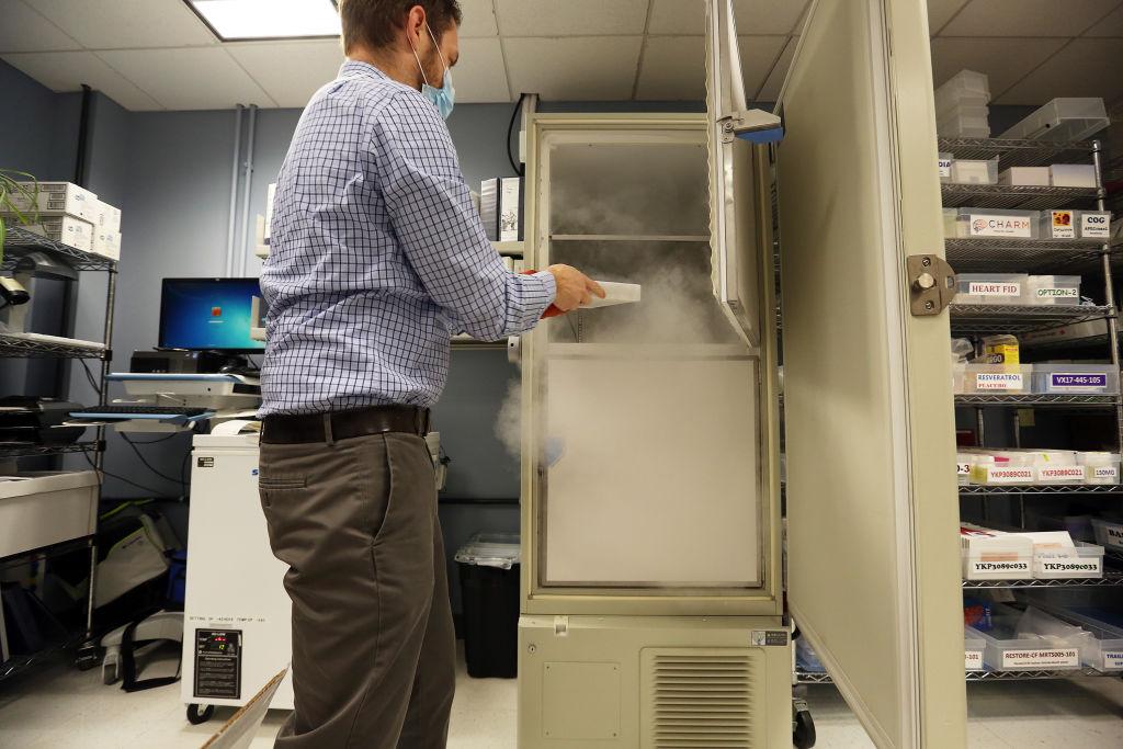 A man wearing a mask removing a tray of vaccine doses from an ultra-low temperature refrigerator.