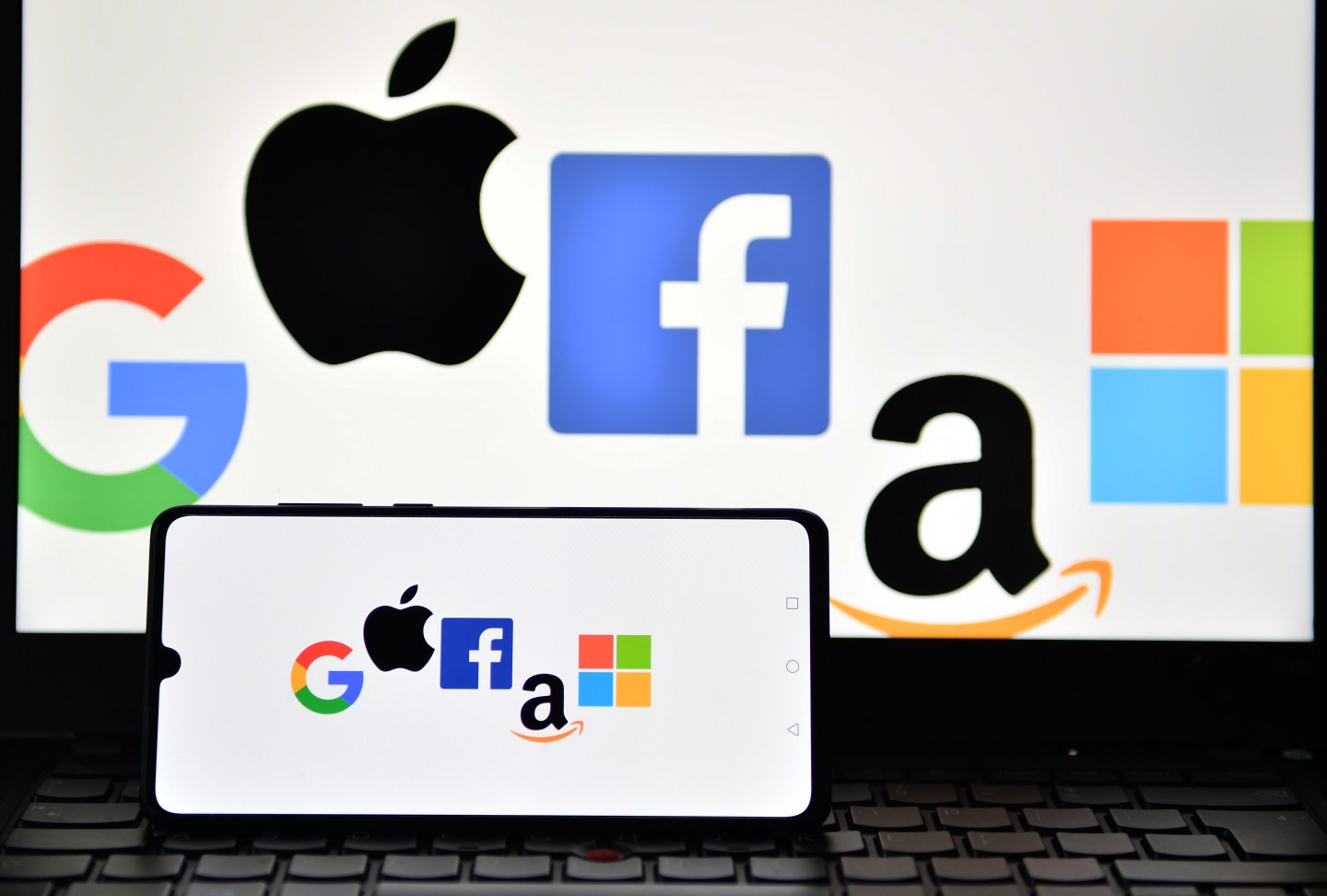 An illustration picture taken in London on December 18, 2020 shows the logos of Google, Apple, Facebook, Amazon and Microsoft displayed on a mobile phone and a laptop screen.