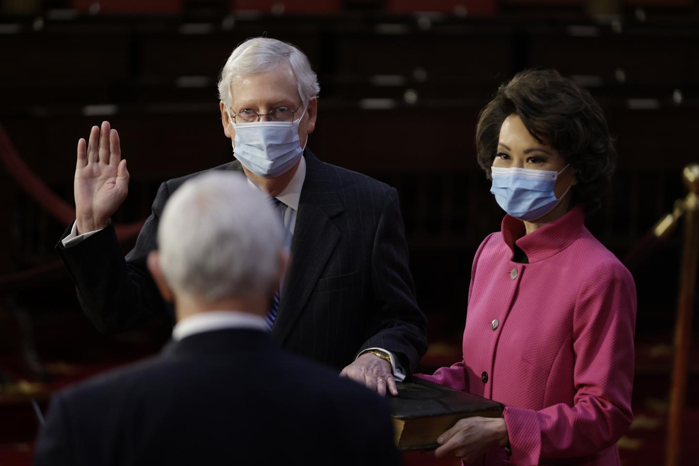 Senate Majority Leader Mitch McConnell, a Republican from Kentucky, left, wears a protective mask while being ceremoniously sworn-in by U.S. Vice President Mike Pence, bottom left, with Elaine Chao, U.S. secretary of transportation, right, at the U.S. Capitol in Washington, D.C., U.S., on Sunday, Jan. 3, 2021.
