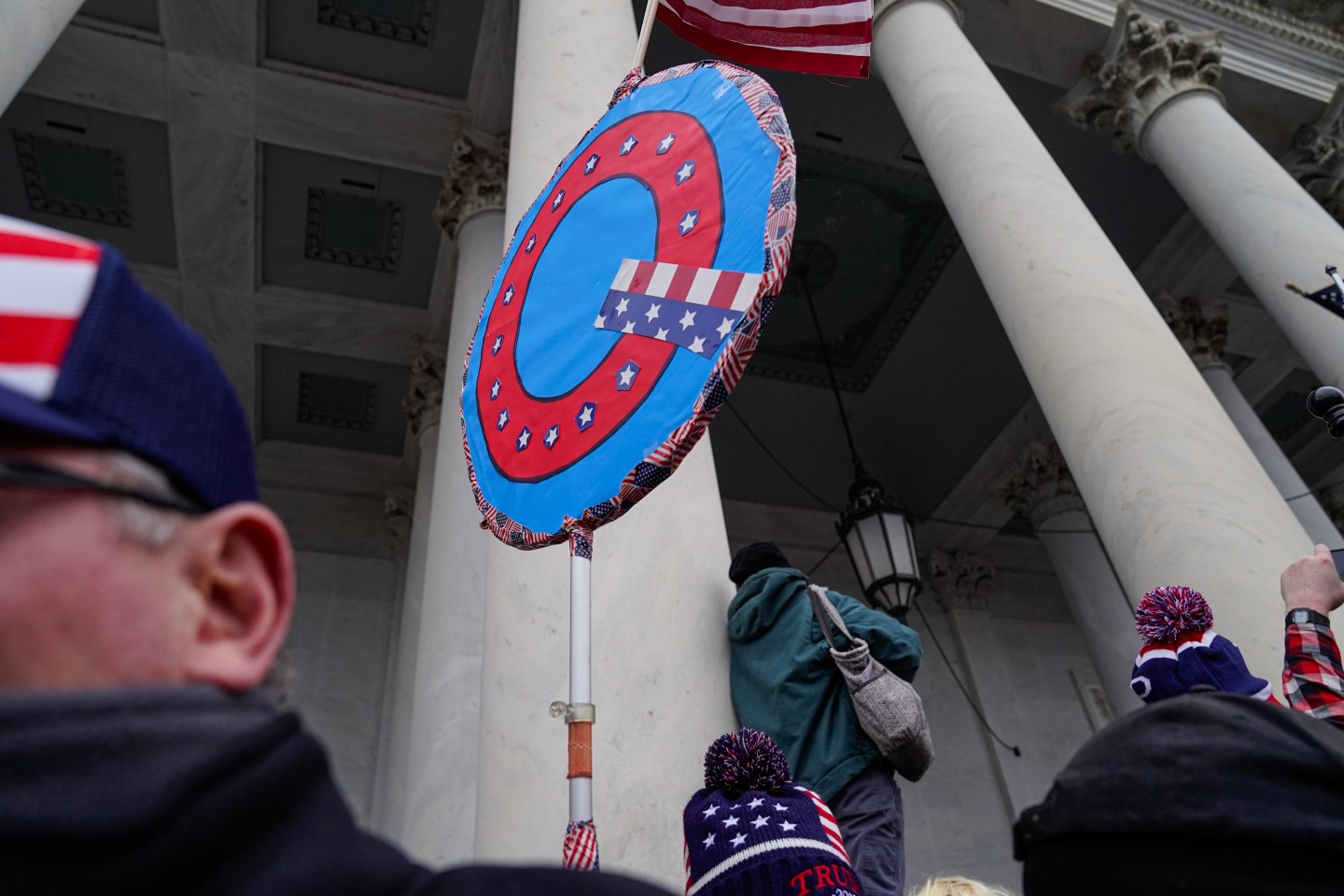 Trump supporters hold up a QAnon banner at a protest outside the U.S. Capitol on Jan. 6. “Raising the ‘prices’ conspiracy theorists pay for their fantasies, within the bounds of First Amendment protections and consistent with common decency, will help rein in the costs they impose on others,” writes Ryan Young.