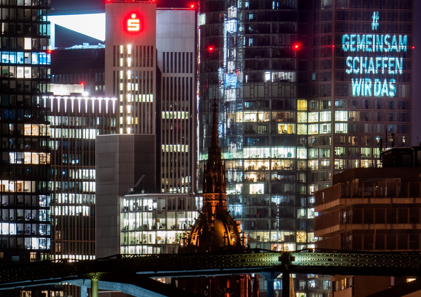 04 February 2021, Hessen, Frankfurt/Main: The light projection #gemeinsamschaffenwirdas can be seen in the evening on the Main Tower (r.o.), the main building of Landesbank Hessen-Thüringen (Helaba), among other Frankfurt skyscrapers.