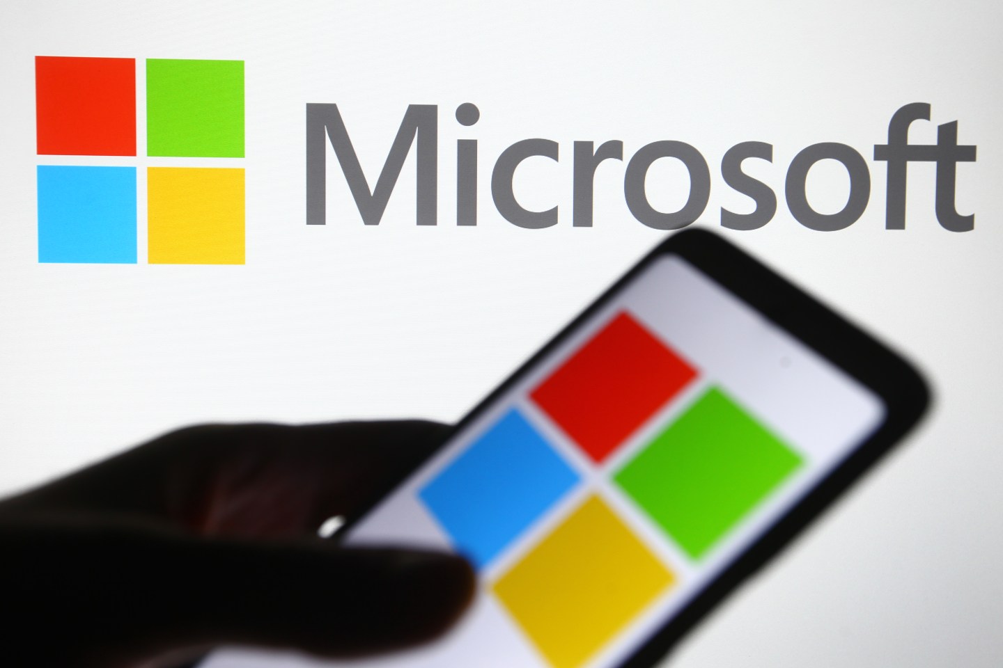 In this photo illustration a Microsoft logo is seen on a mobile phone and a pc screen.