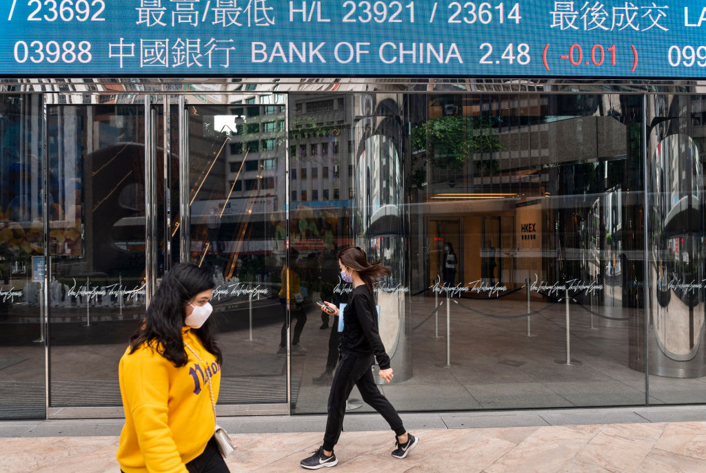 Pedestrians walk past a stock market display board showing