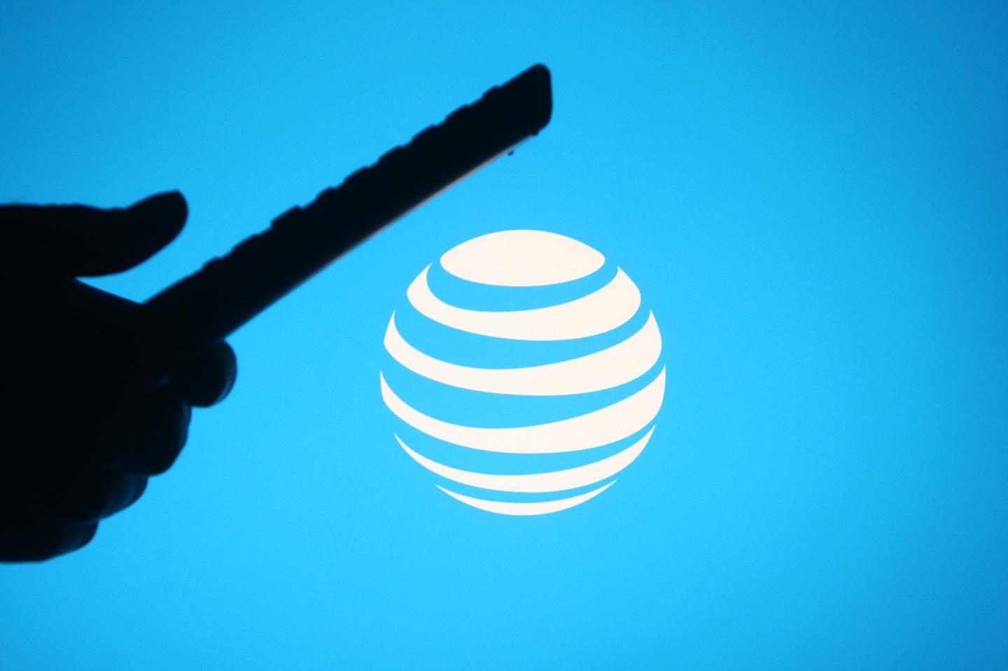 In this photo illustration the AT&amp;T logo is seen behind a silhouette hand holding a tv remote.