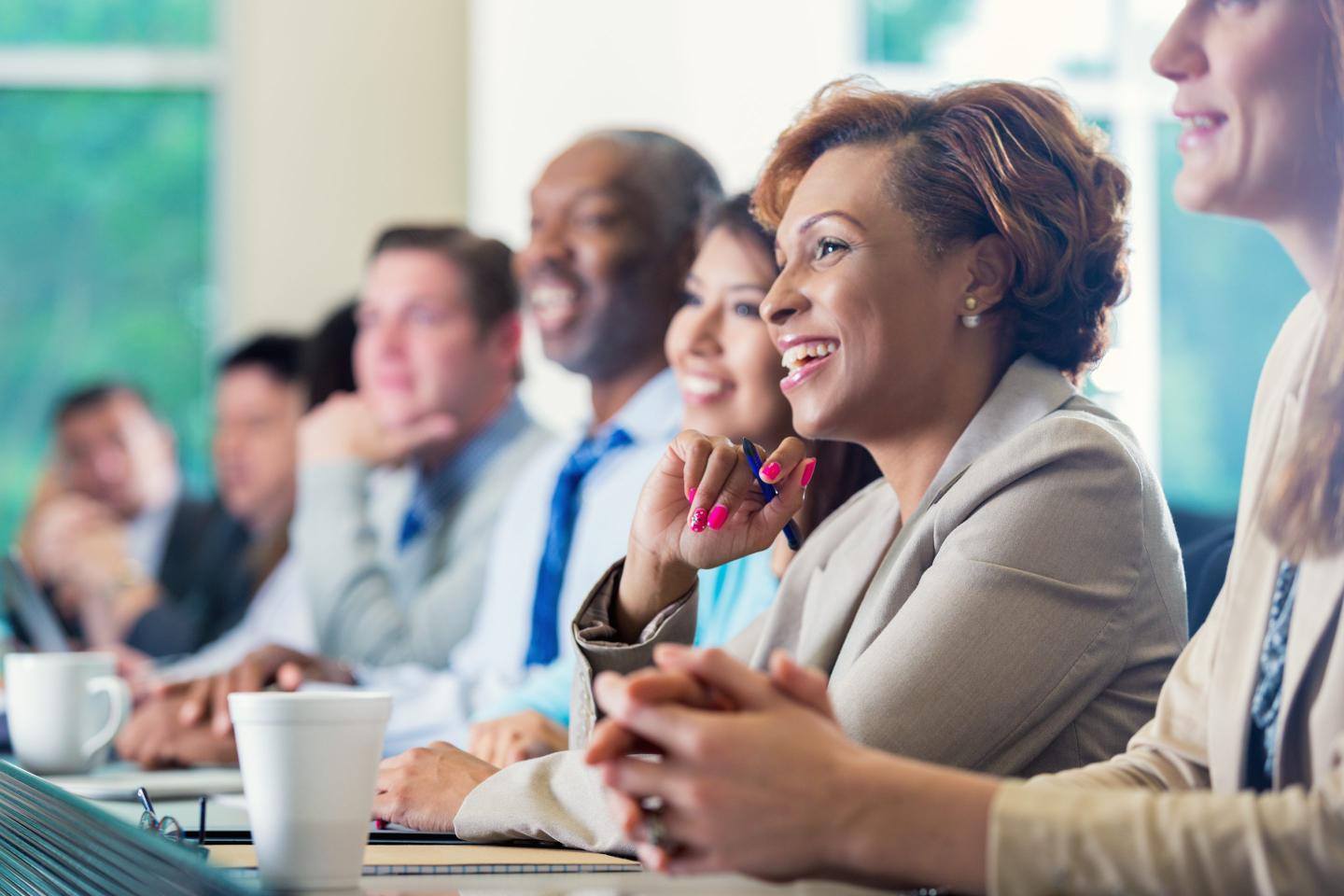 Woman attends business seminar, sitting at long table among other leaders.